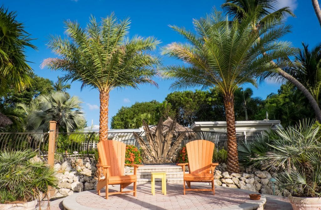 Two bright orange deck chairs in front of two short palm trees under a blue sky at the Kona Kai Resort in Key Largo