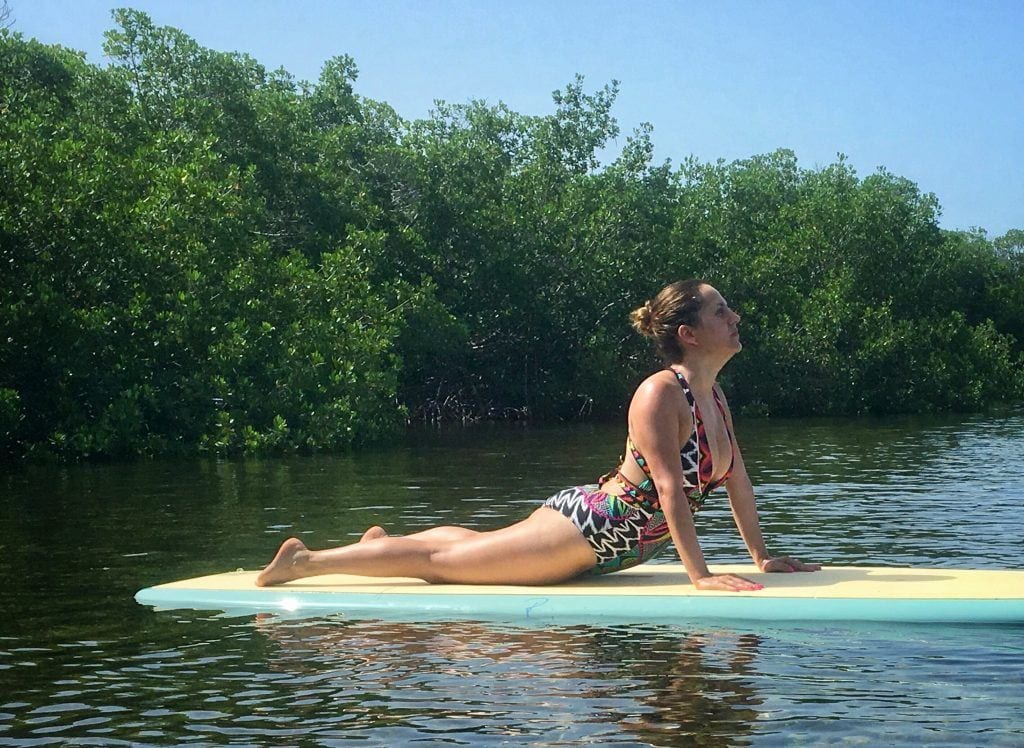 Kate doing cobra yoga pose on a paddle board in the water, surrounded by mangroves.