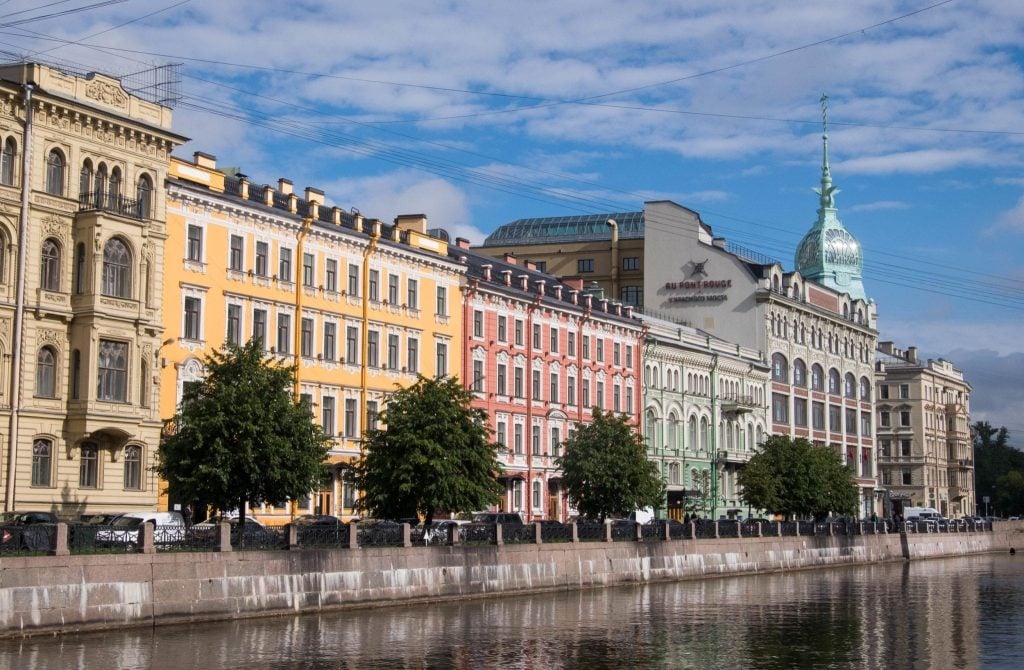 Buildings in St. Petersburg along the river, in the colors of yellow, salmon pik, and mint green.