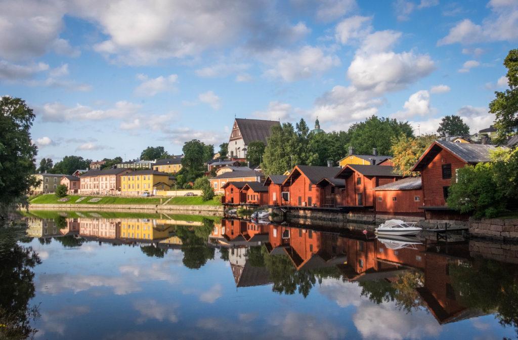Red little cottages on a lake reflecting the blue and white cloudy sky in Porvoo, Finland.