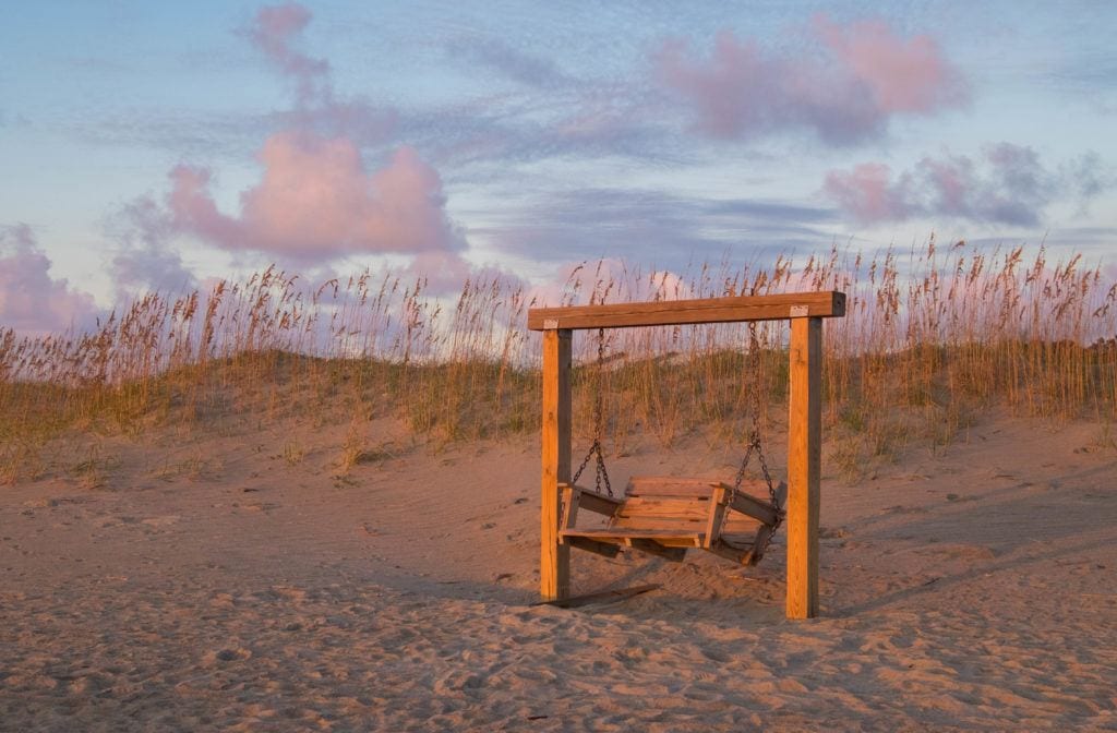 An empty swinging bench on the beach at sunrise on Tybee Island.