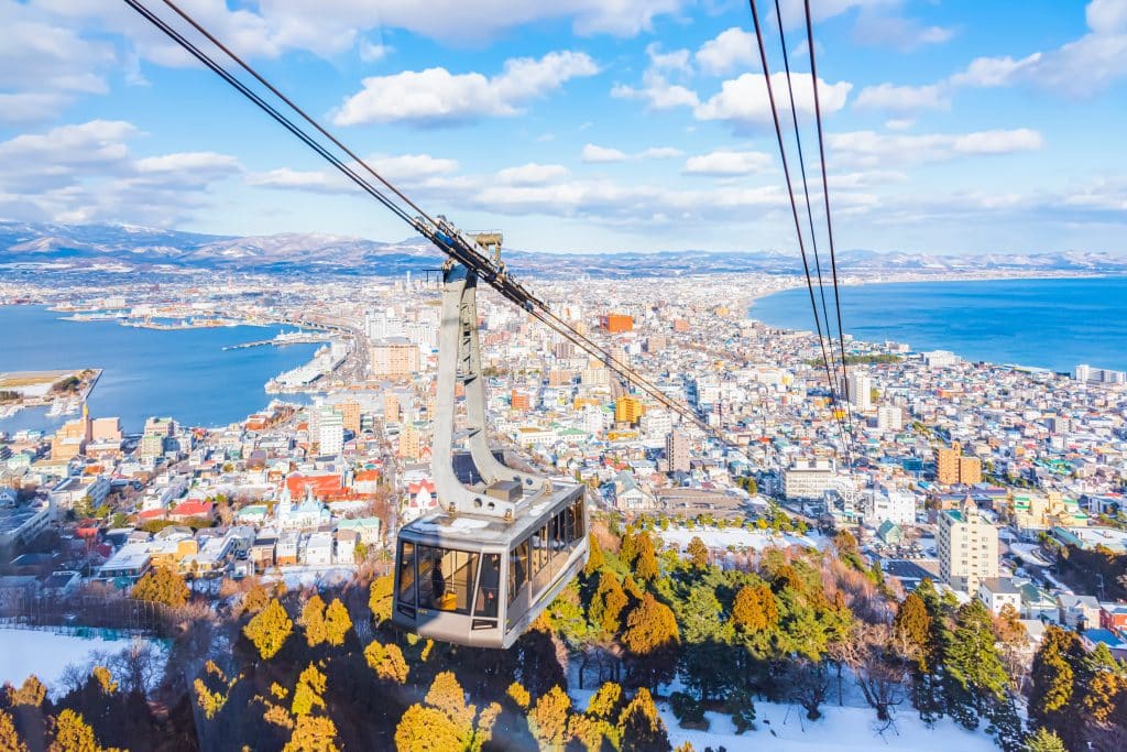 A cable car traveling up a hill from a snowy city in Japan.