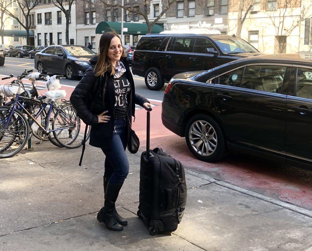 Kate standing with a black suitcase on the street in New York.