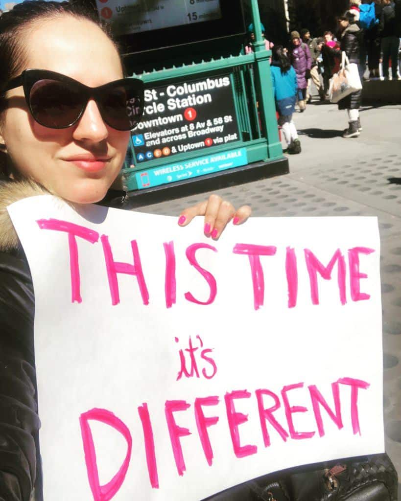 Kate holding a protest sign that says "This time it's different"