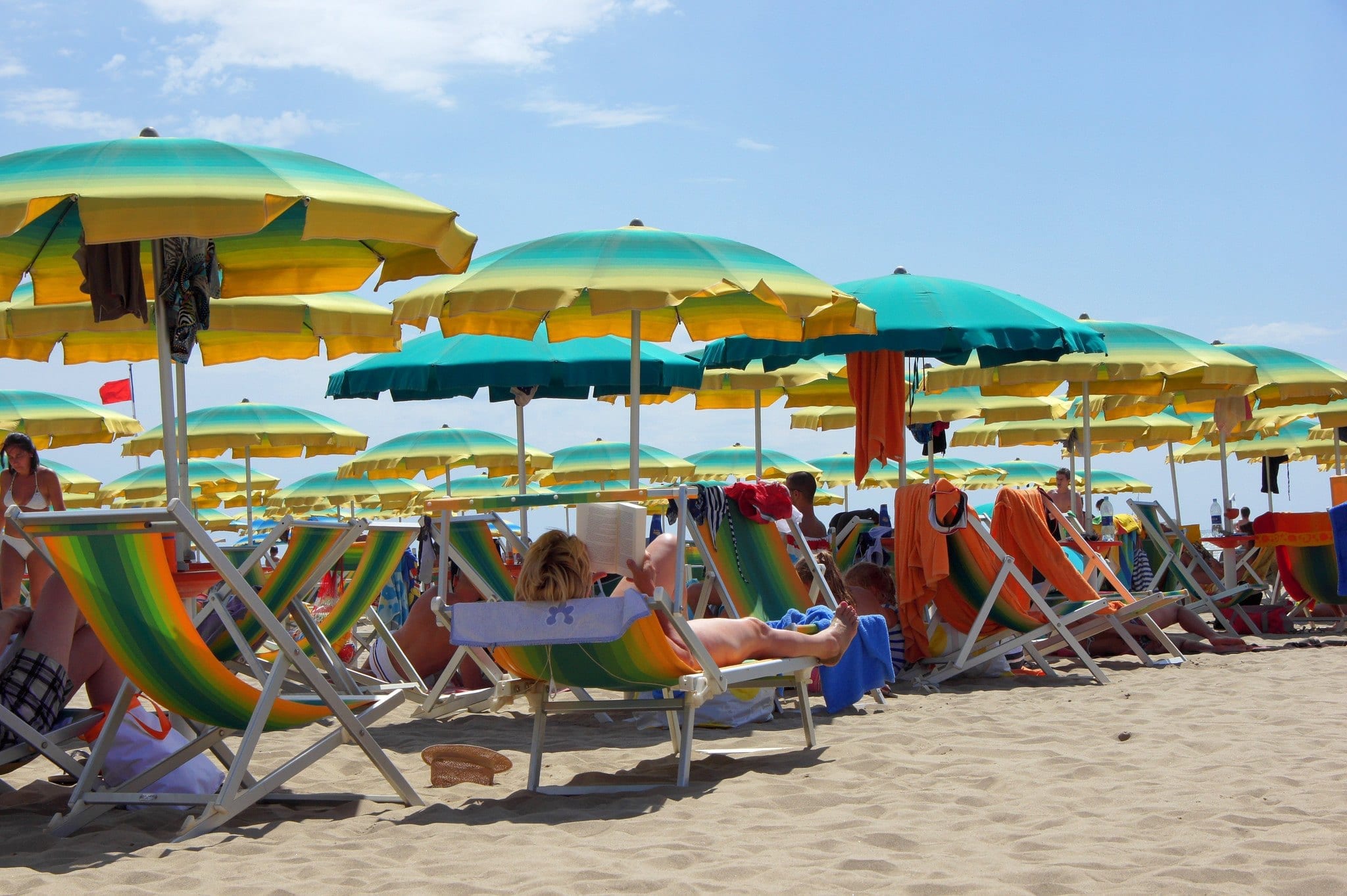People lounging in colorful blue and yellow beach chairs with umbrellas in Viareggio Italy. 