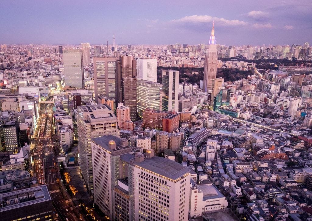 A view from above over Tokyo with lots of skyscrapers, in a pink sky.