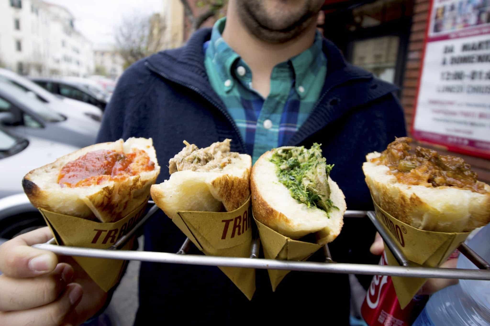 A man holds up four cones of what looks like bread topped with sauce in Rome.