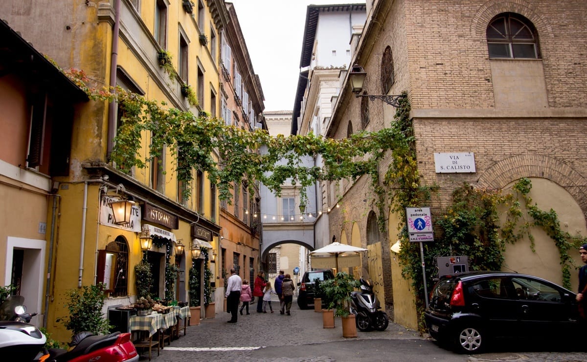 A quiet side street in Trastevere, Rome, with yellow painted buildings and ivy-covered arches, fairy lights in the background.