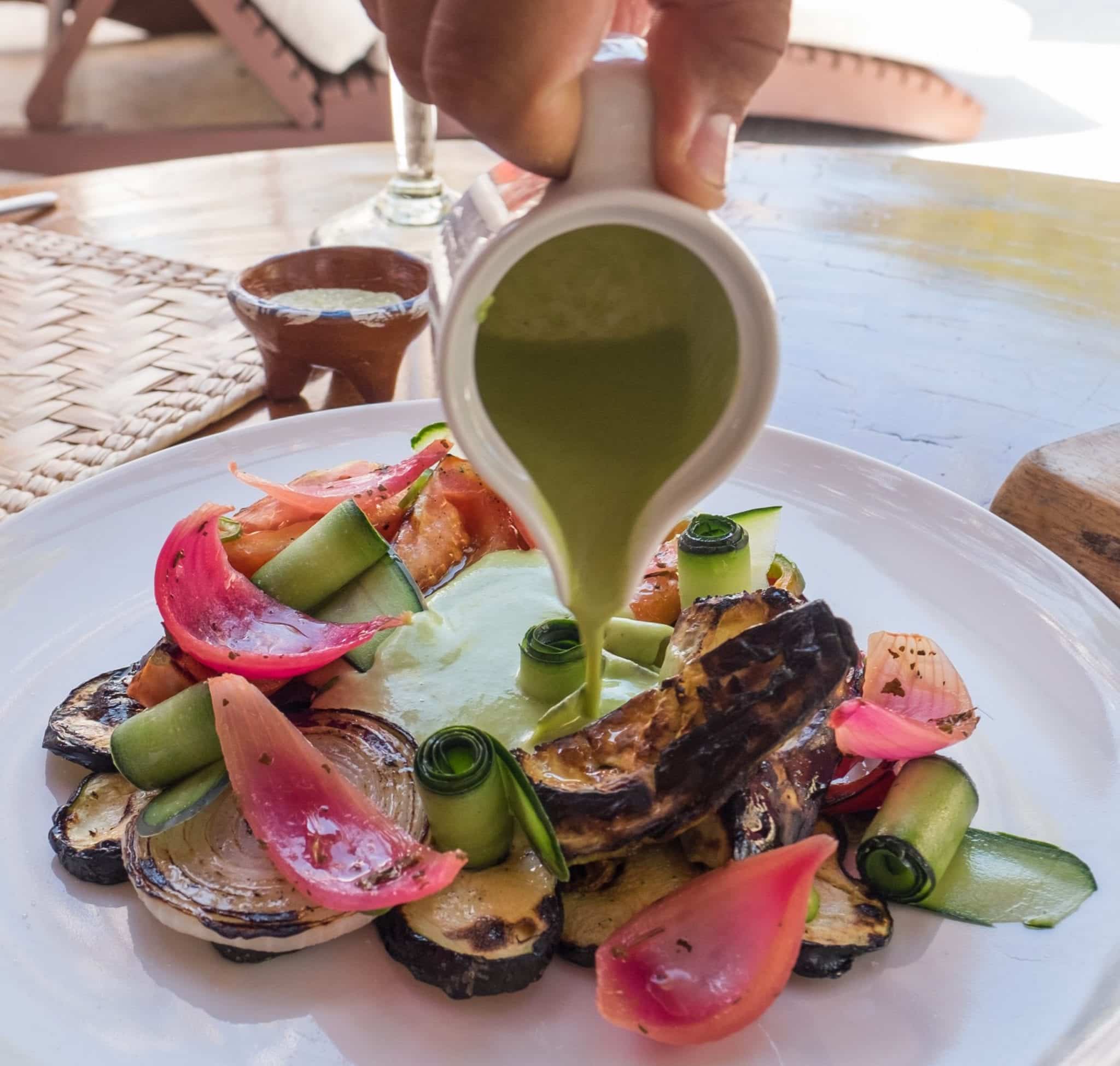 Closeup of grilled vegetables on a plate with green sauce being poured on top.