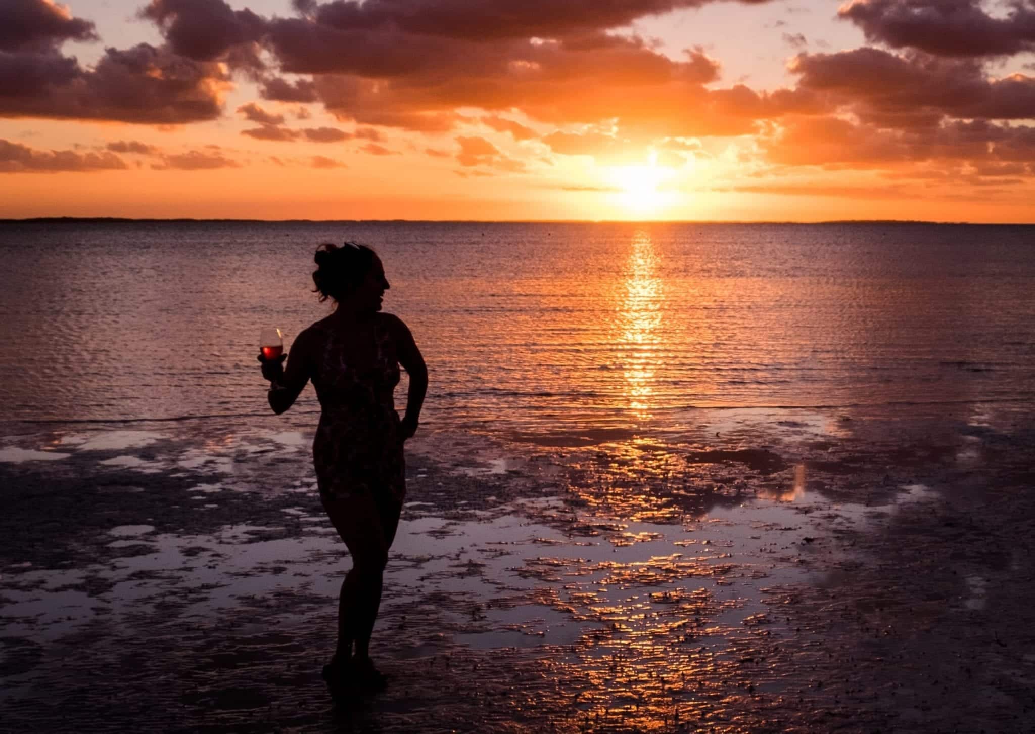 Woman holding wine glass, posing in front of the water at sunset.