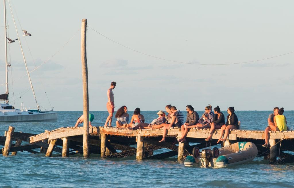 People sitting on a long pier dipping into the ocean.