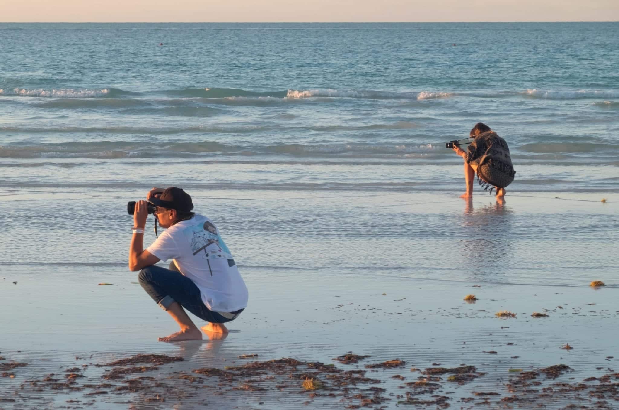 Two people holding cameras and taking photos on the beach.