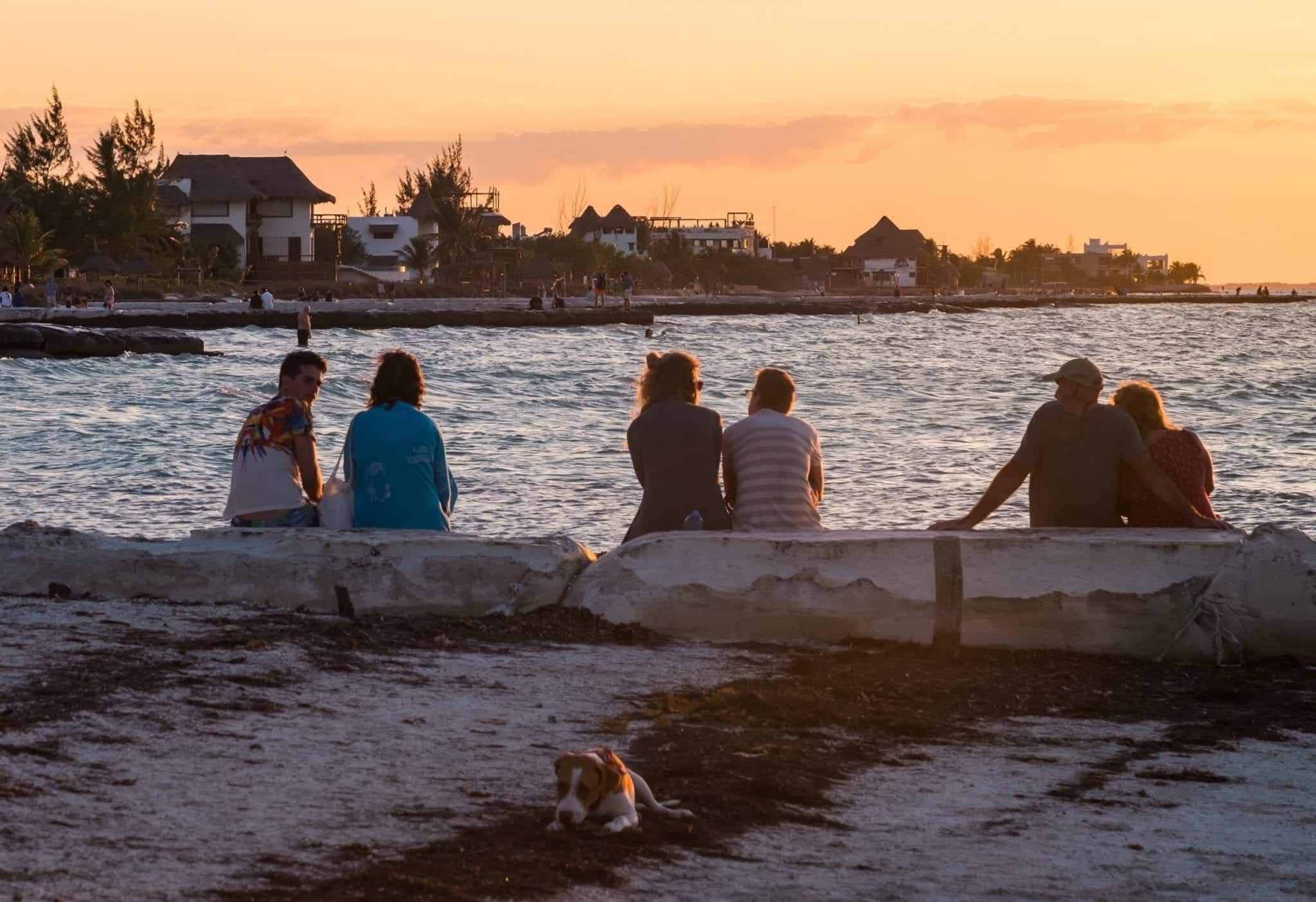 People sitting on the sea wall watching sunset.