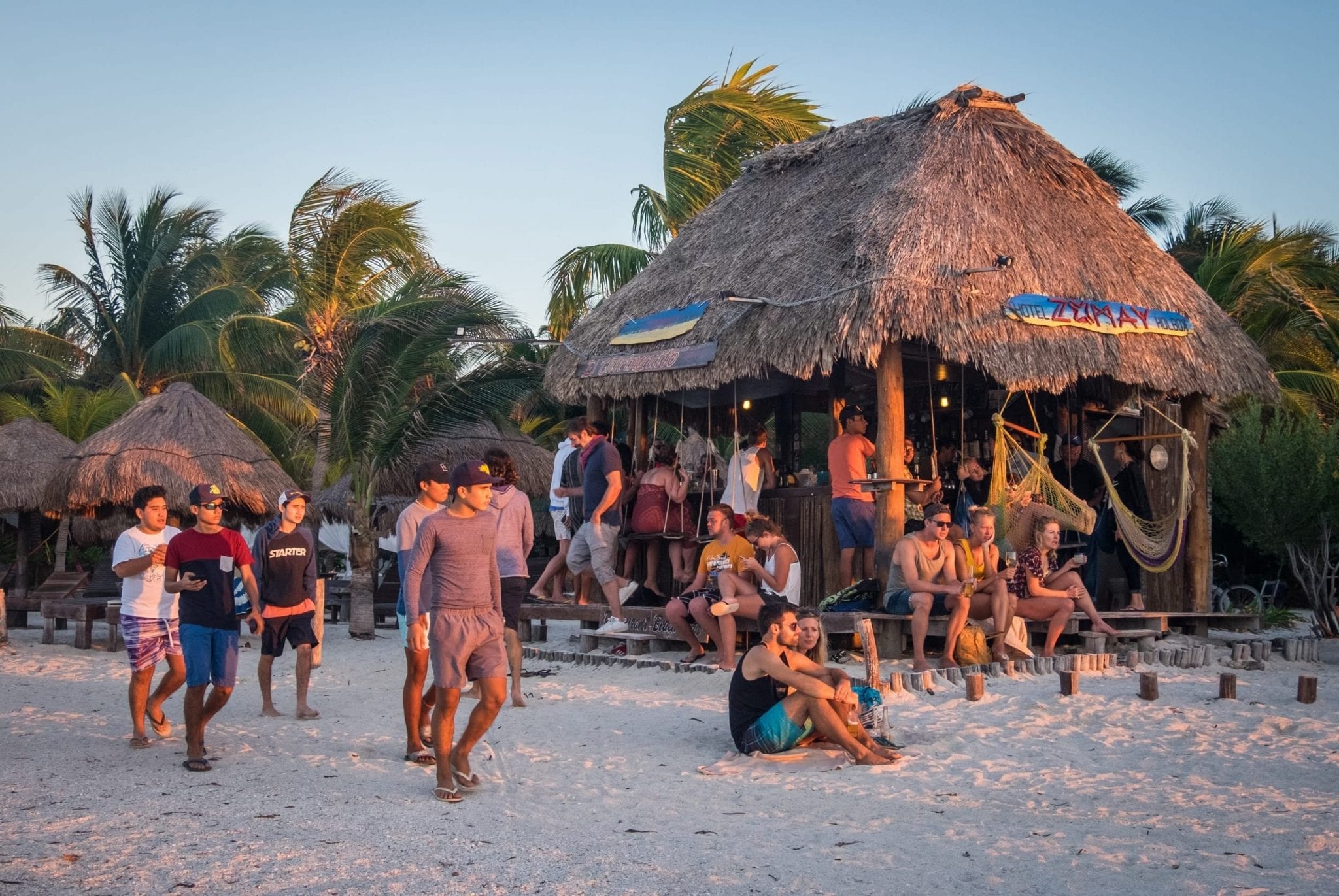 Several people at a beach bar sitting on swings and benches.