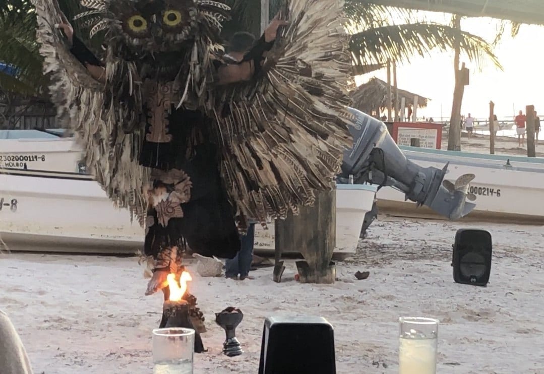 Man dancing in owl costume and holding his foot over fire.