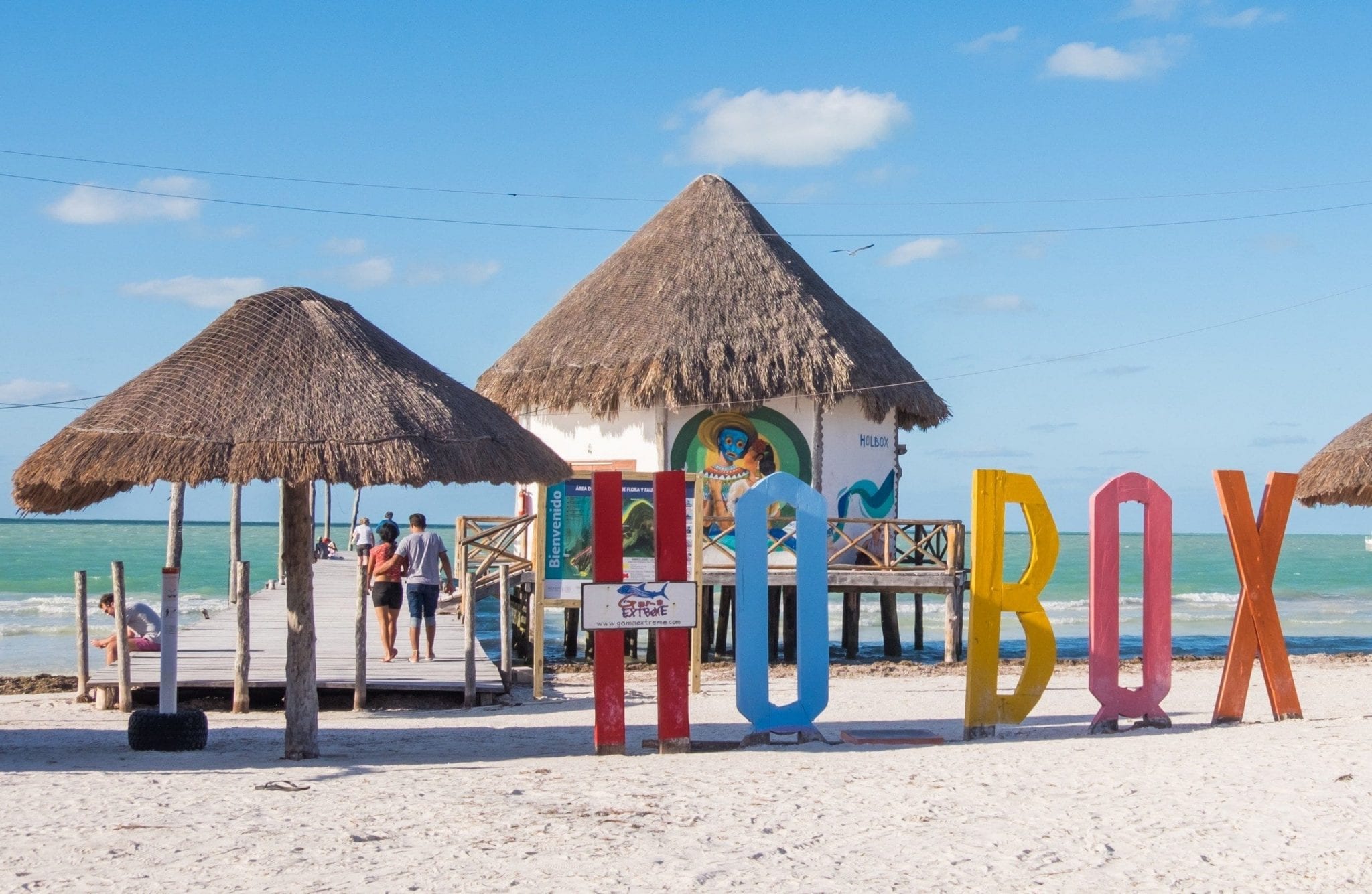 Bright letters reading "Holbox" in front of palapas and the turquoise ocean.