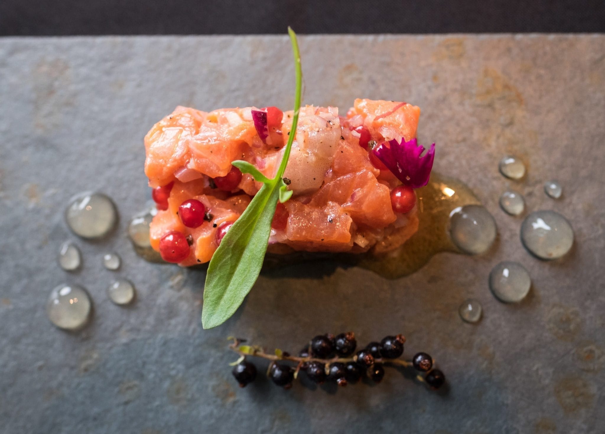 Raw salmon tartare on a plate with berries and vinegar bubbles.