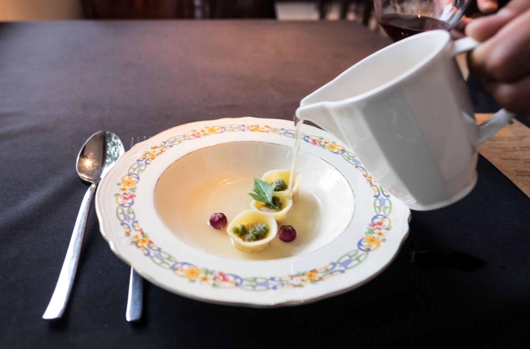 A plate with three pieces of round pasta in it, and a hand pouring in soup from a cup.