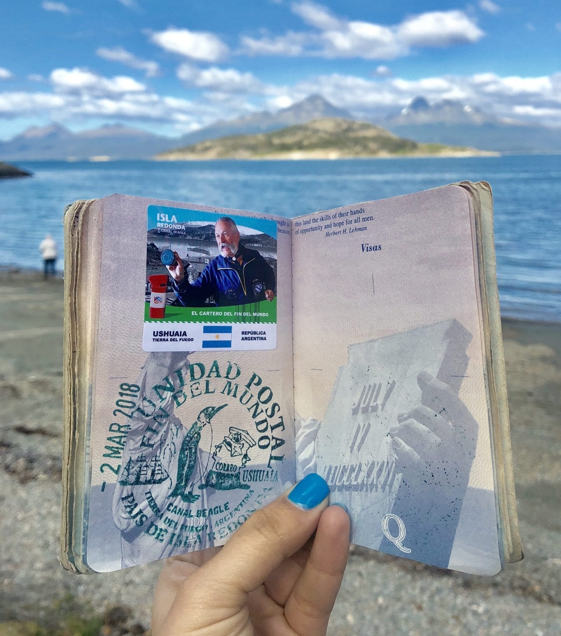 A passport covered with a giant souvenir stamp reading Fin Del Mundo with a penguin on it.
