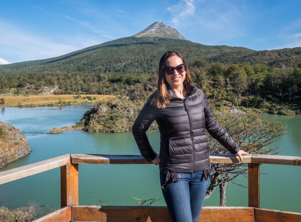 Kate stands in front of a bright green lake in Ushuaia with a mountain behind it.