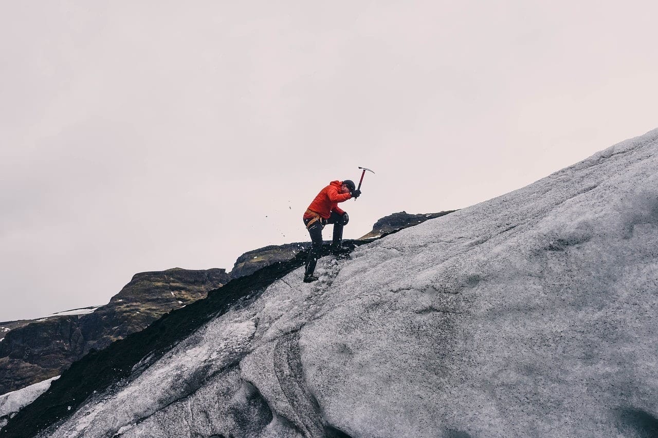 A man hiking a glacier, pickaxe in hand.