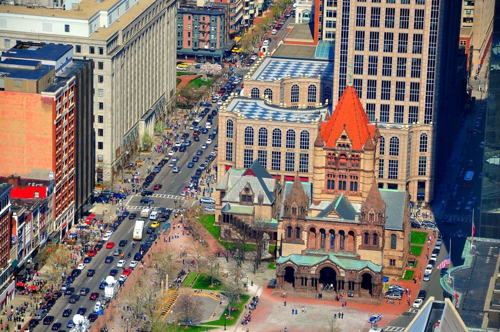 An aerial shot of a brick church set amongst tall skyscrapers.