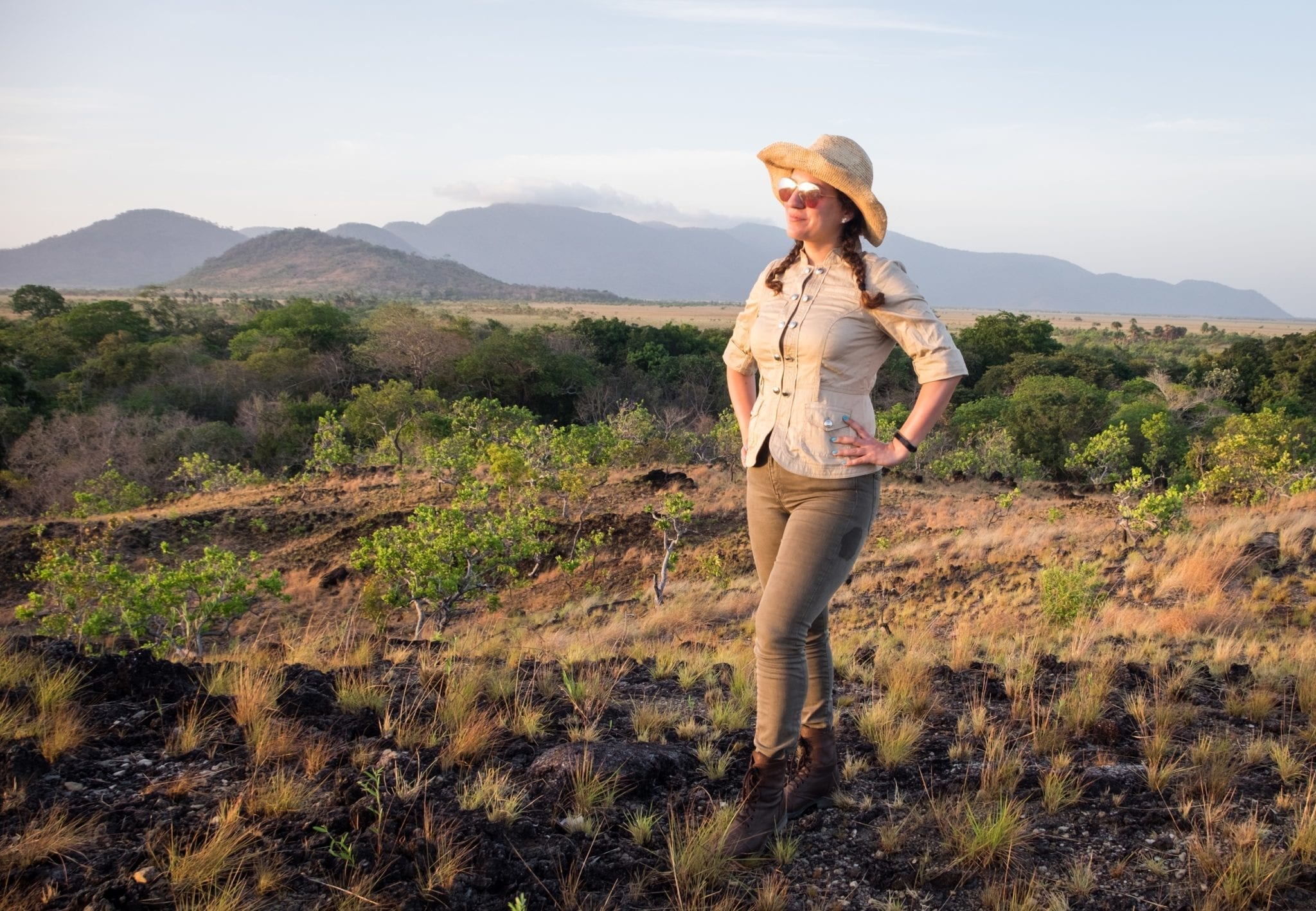 Kate in Saddle Mountain, Rupununi, Guyana Kate wearing a tan jacket and green pants and boots, and a hat, looking out over the savannah grasslands in the Rupununi of Guyana.