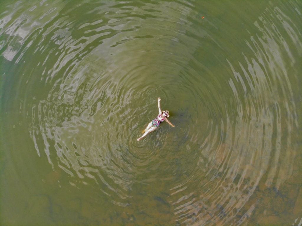 A drone shot of Kate swimming in the bright-green creek from way up high.