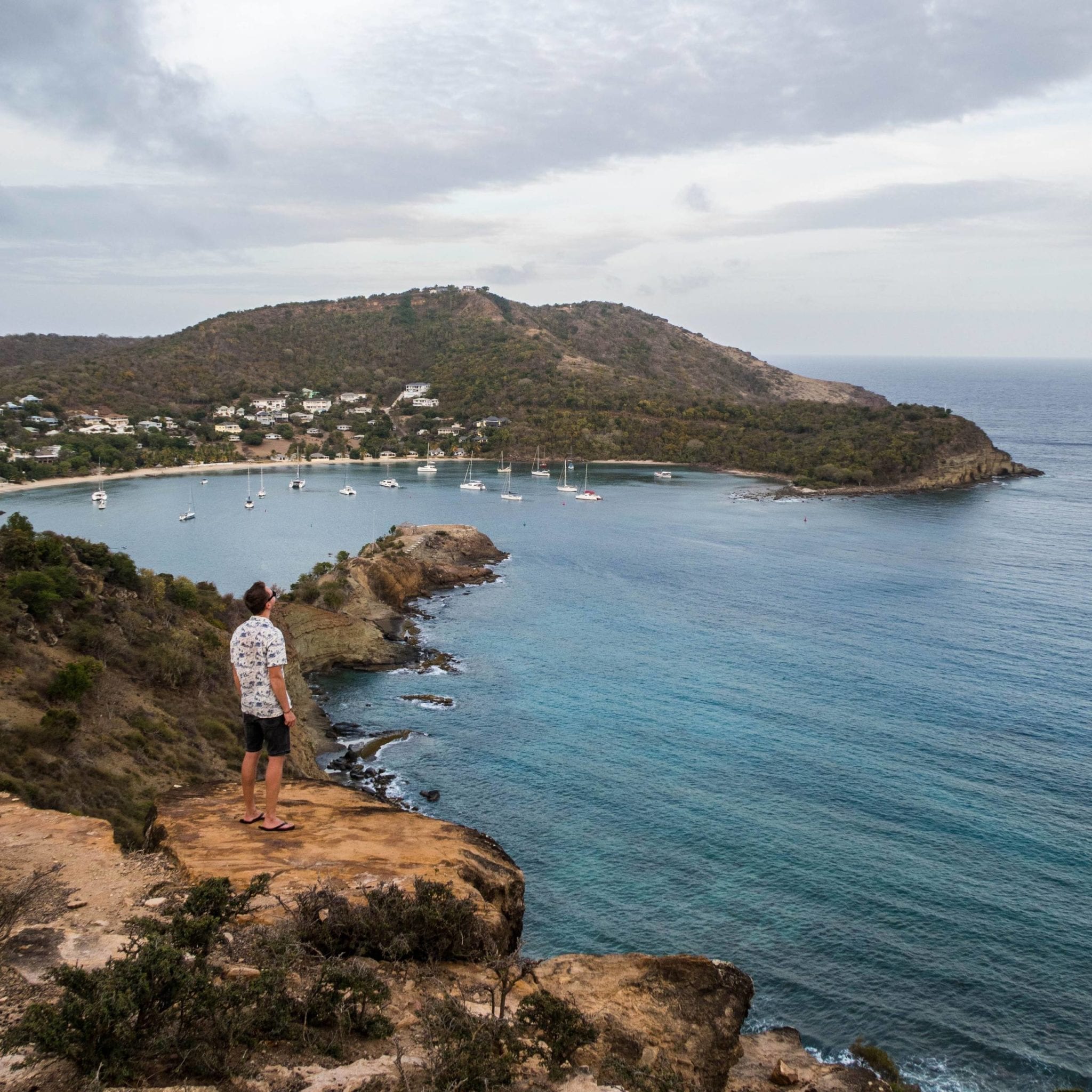 Patrick standing on the edge of a cliff, looking on to the English Harbour in Antigua.