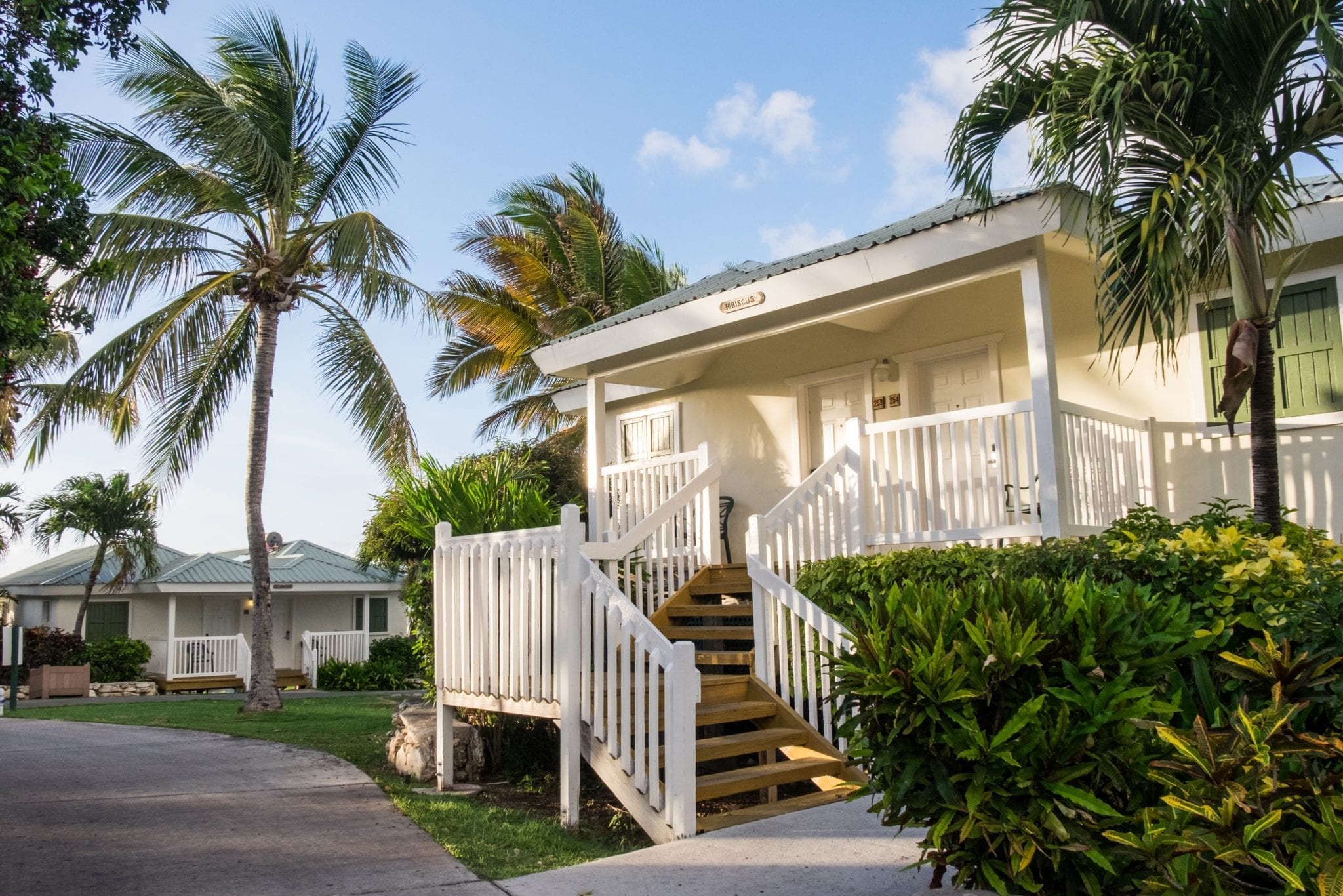 A small White House with picket fencing along the staircase leading upward, surrounded by palm trees underneath a blue sky.