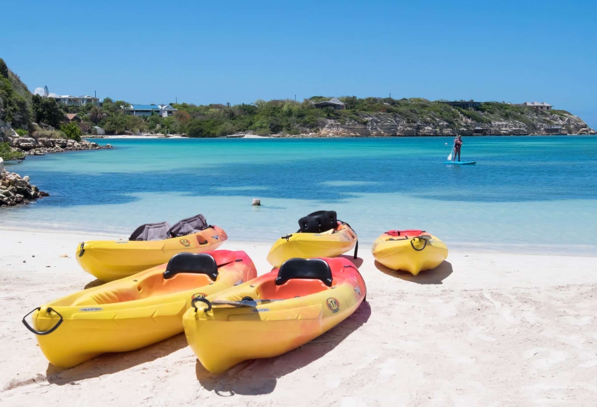 Several yellow and red kayaks resting on a white sand beach in front of a turquoise ocean.