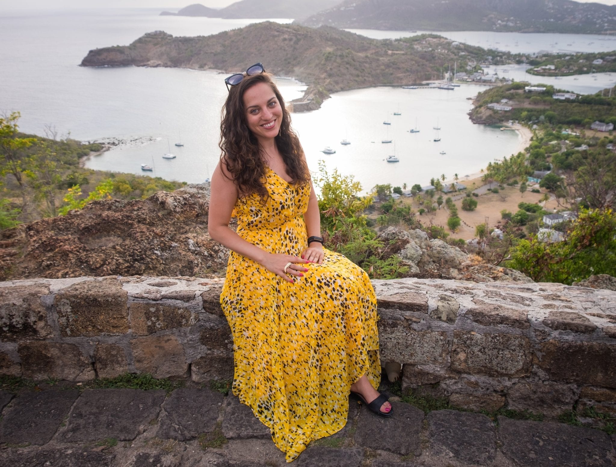 Kate sitting on a short wall in a long gauzy yellow and black gown. In the background is a view over the White Sea down below, and mountains in the distance.