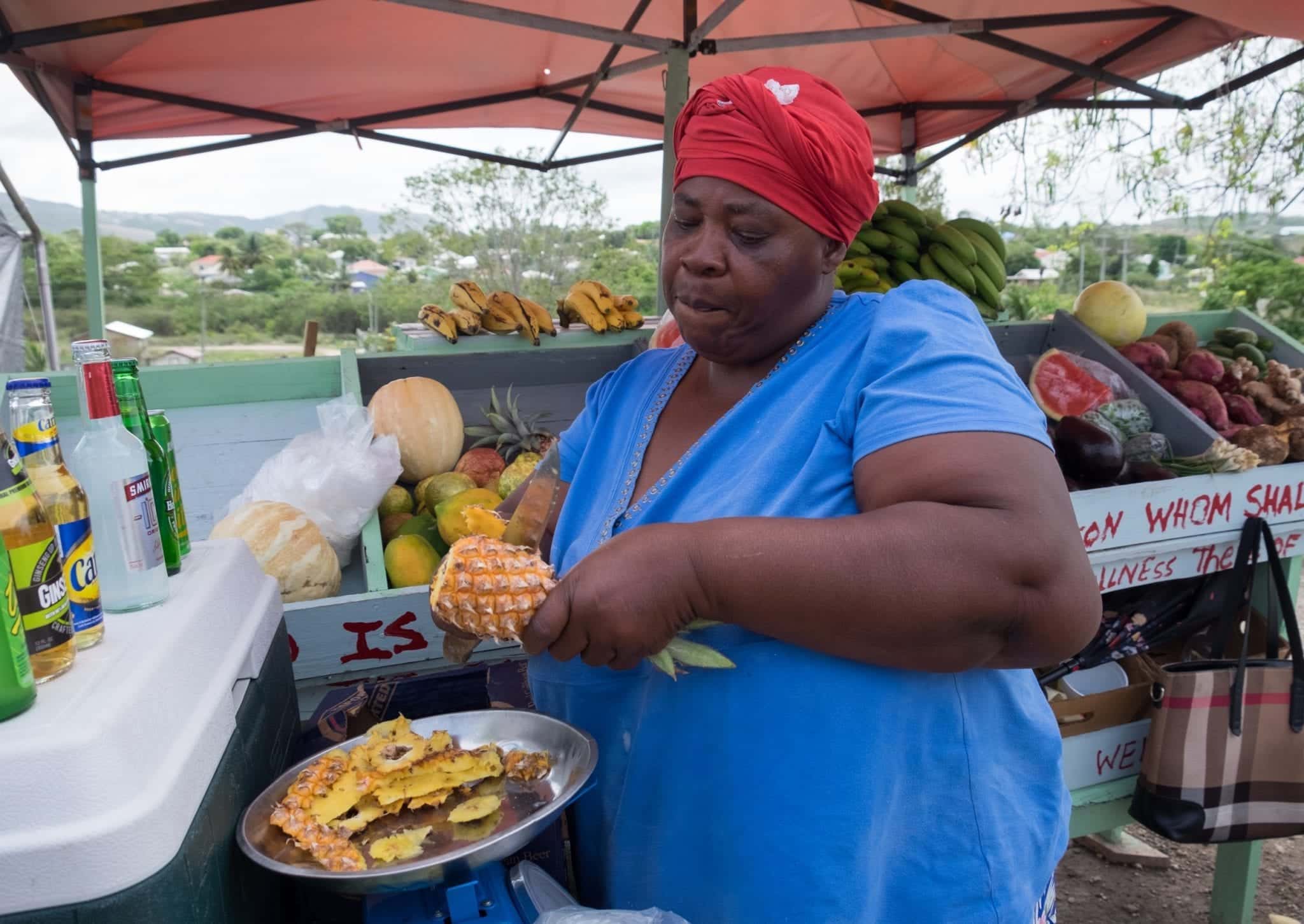 A woman in a red bandana slices a pineapple into a plastic bag in Antigua.