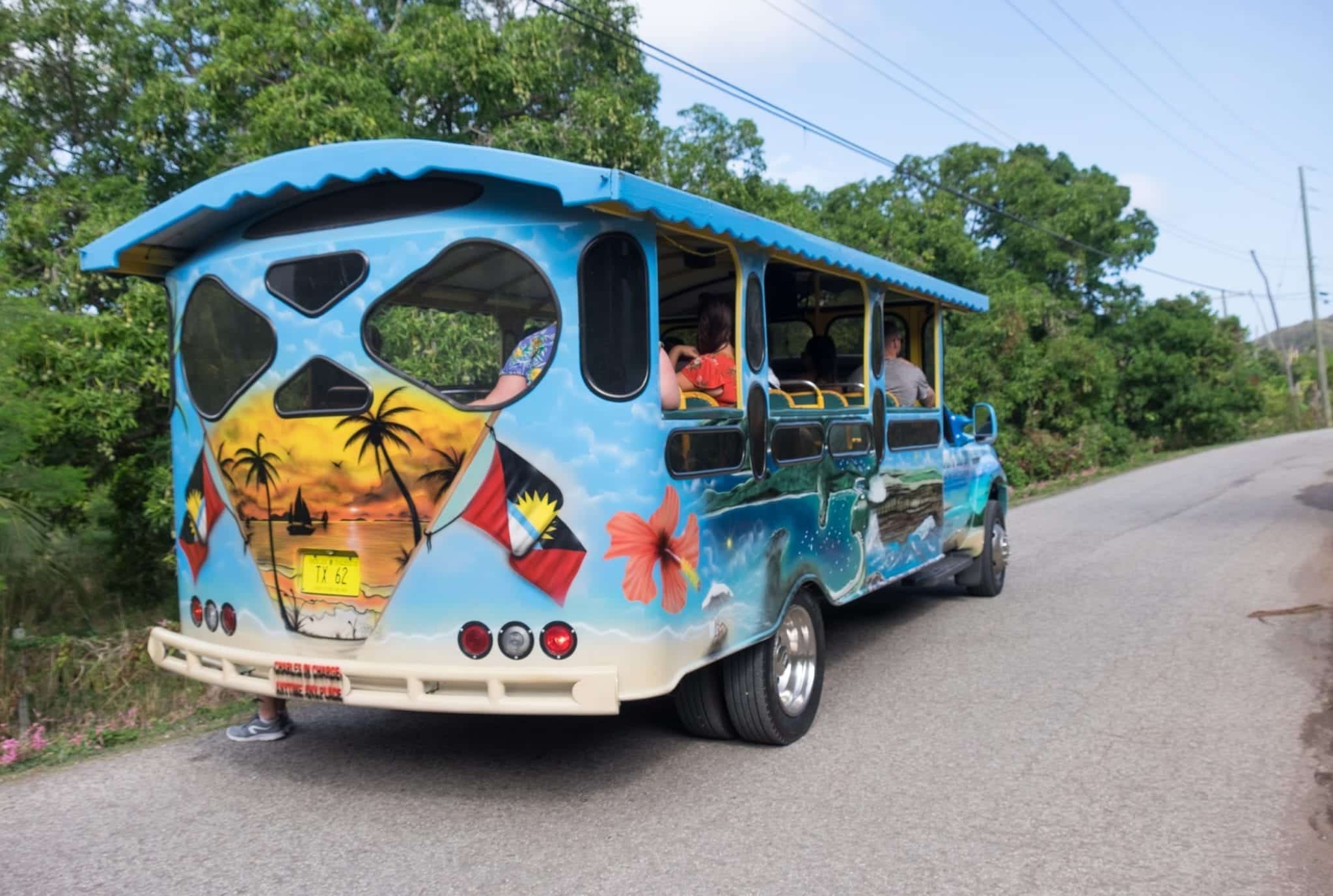 The back of a brightly painted blue bus with orange palm trees painted on the back in Antigua