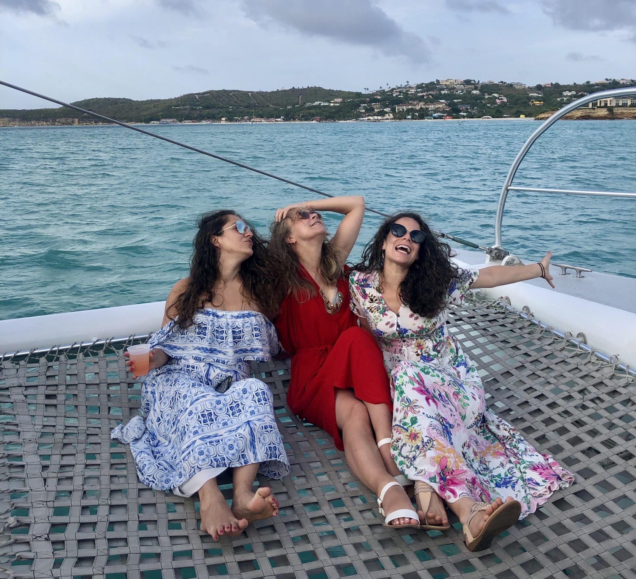 Three girls in floral patterned dresses sitting on the net of the catamaran, looking off to the side and making goofy kissy faces.