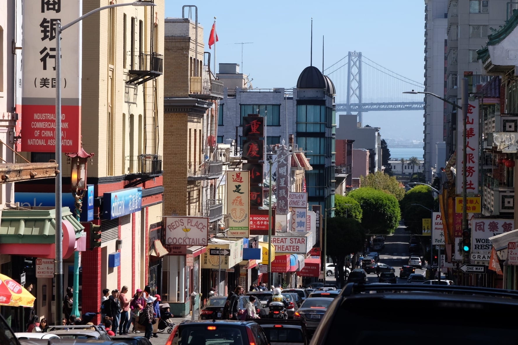 View over Chinatown in San Francisco, lots of store signs jutting out at angles, leading to a bridge underneath a blue sky.