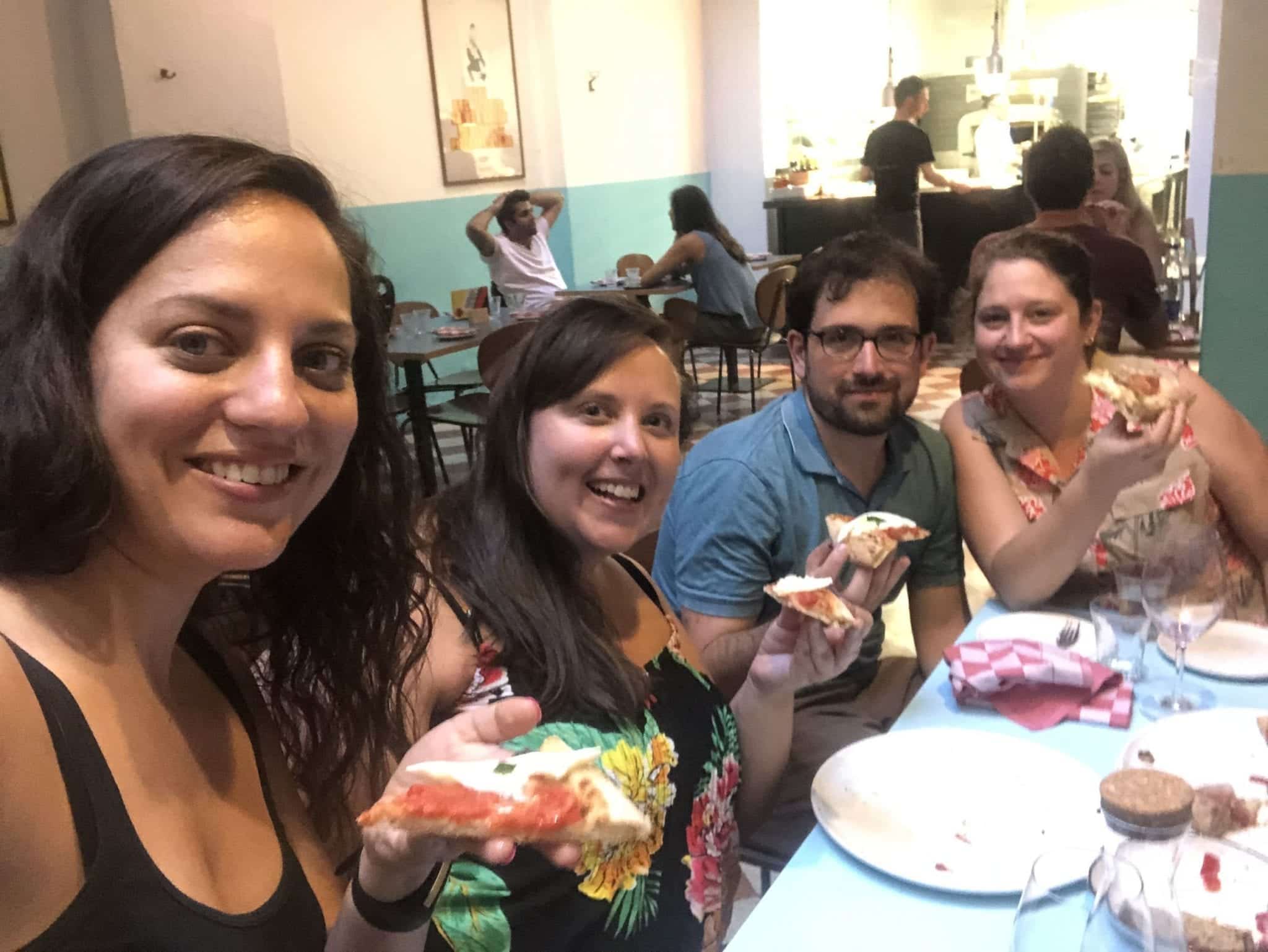 Kate and her friends Cailin, Mike, and Steph pose for a selfie at a pizzeria in Bologna, each holding up a slice of pizza.