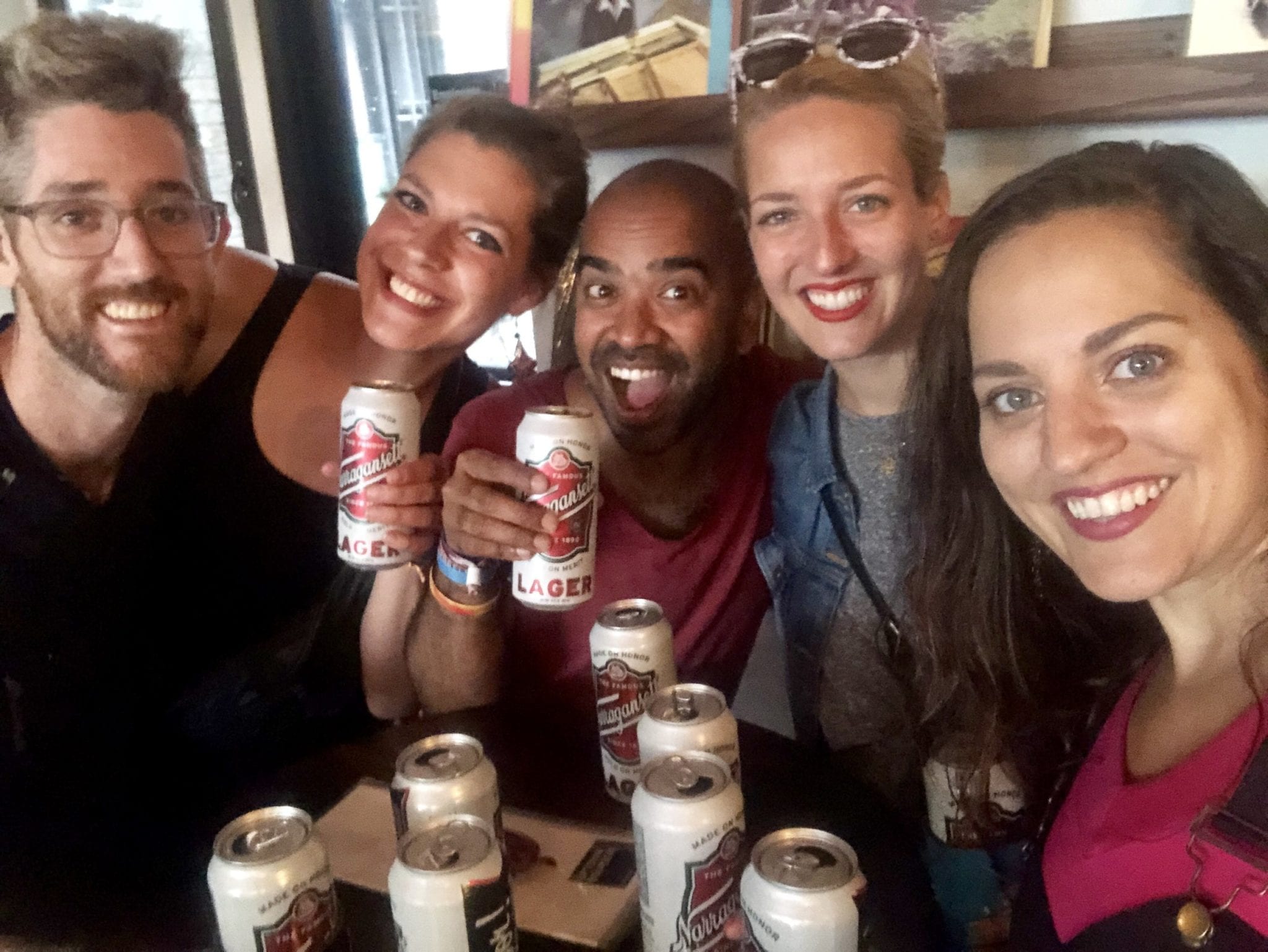 Group selfie: Kate with her friends Sabrina and Kash, her sister Sarah, and her sister's partner Matt, all around a bar table topped with twelve Narraganset tallboy beers.