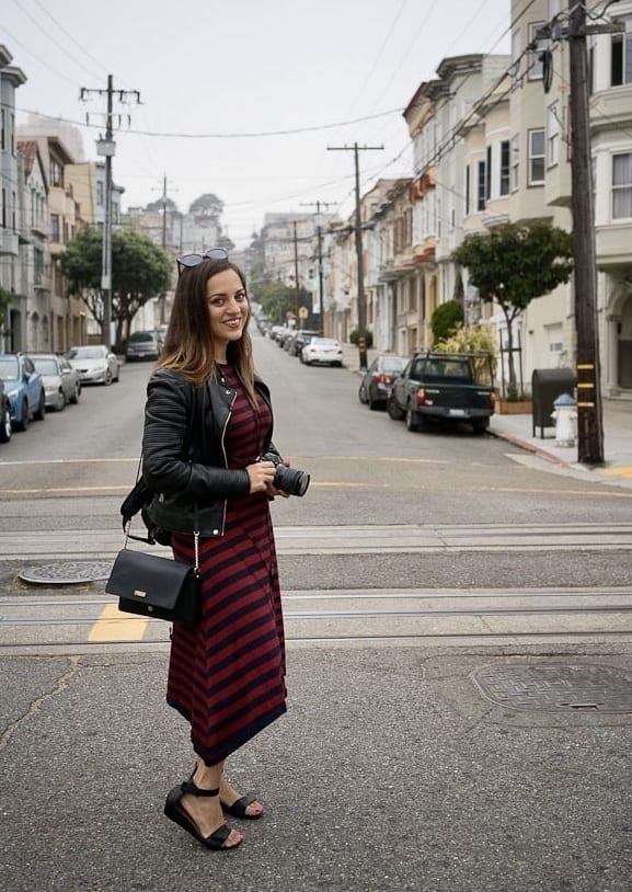 Kate wearing a navy-and-burgundy striped Jason Wu dress, holding a camera in her hand and standing in a gray street in San Francisco early in the morning, houses on both sides.