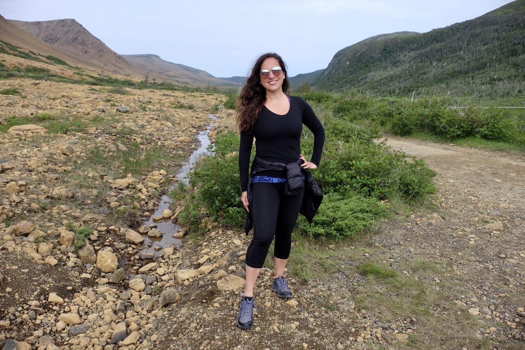 Kate stands in the Tablelands of Newfoundland surrounded by orange rocks and grassy hills.