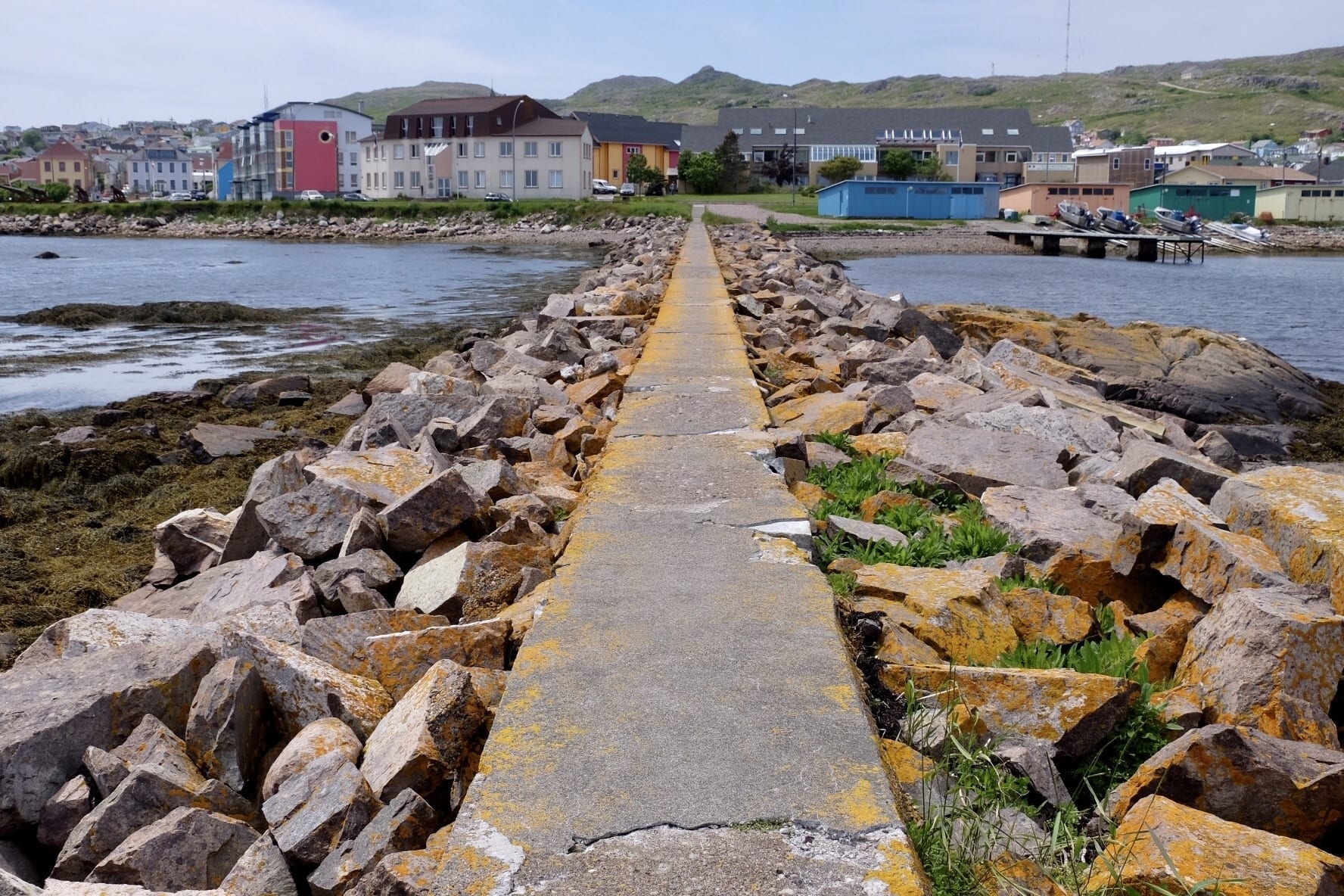 A concrete path with rocks piled on each side leads to the colorful houses of St. Pierre and Miquelon.