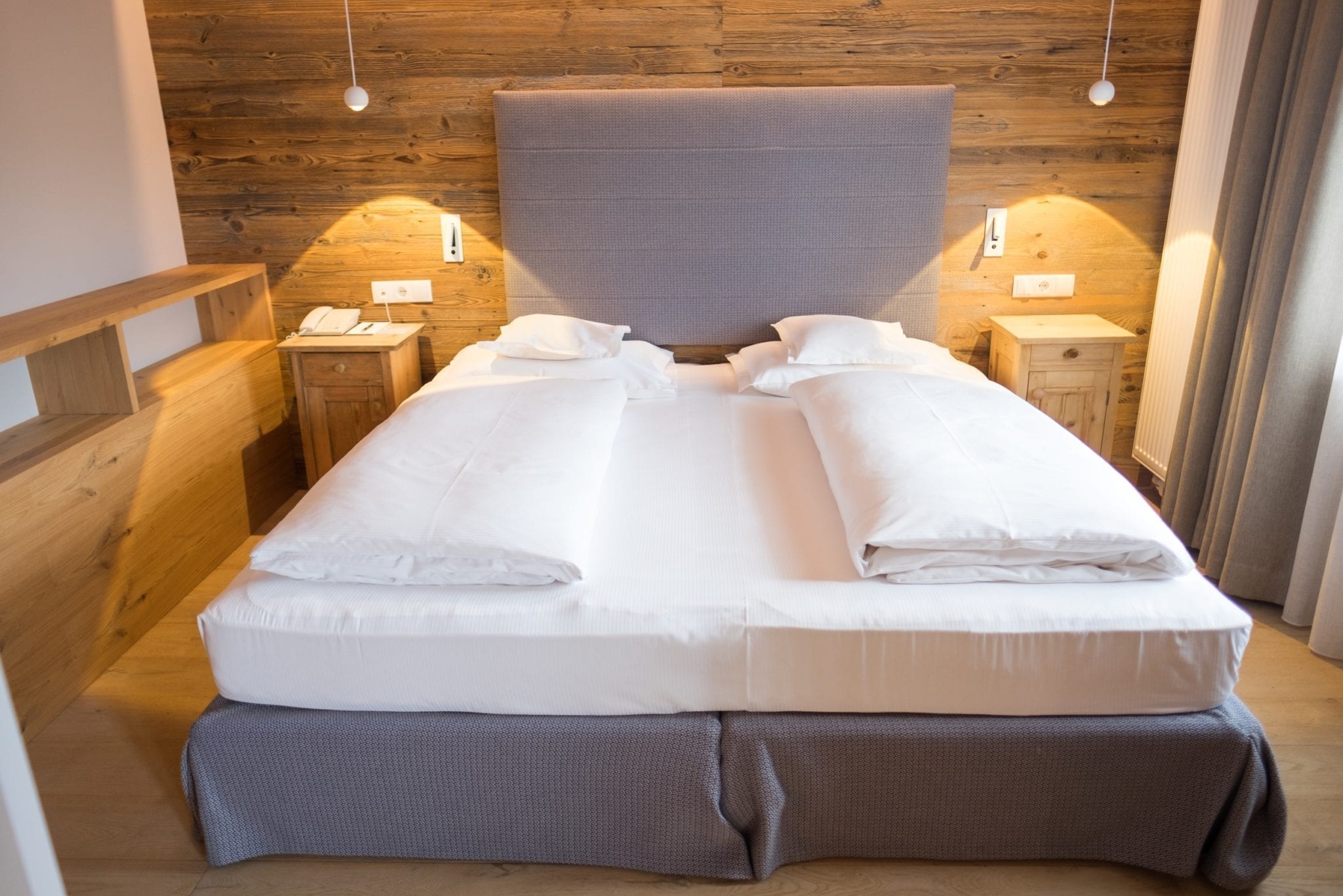 A modern gray bed with two white comforters and small modern lamps on each side.