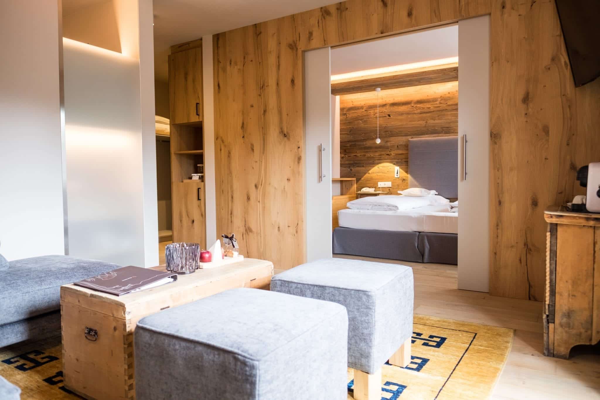 A hotel room with a bed hidden behind a closing wall and two gray ottomans and a coffee table in the foreground.