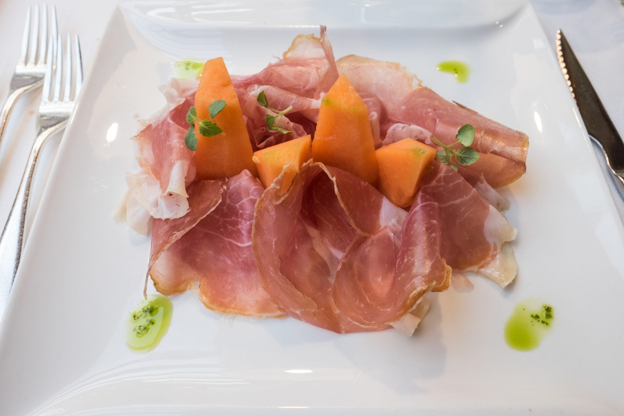 A plate of pillowy pink speck, or Tyrolean ham, with pieces of orange melon.