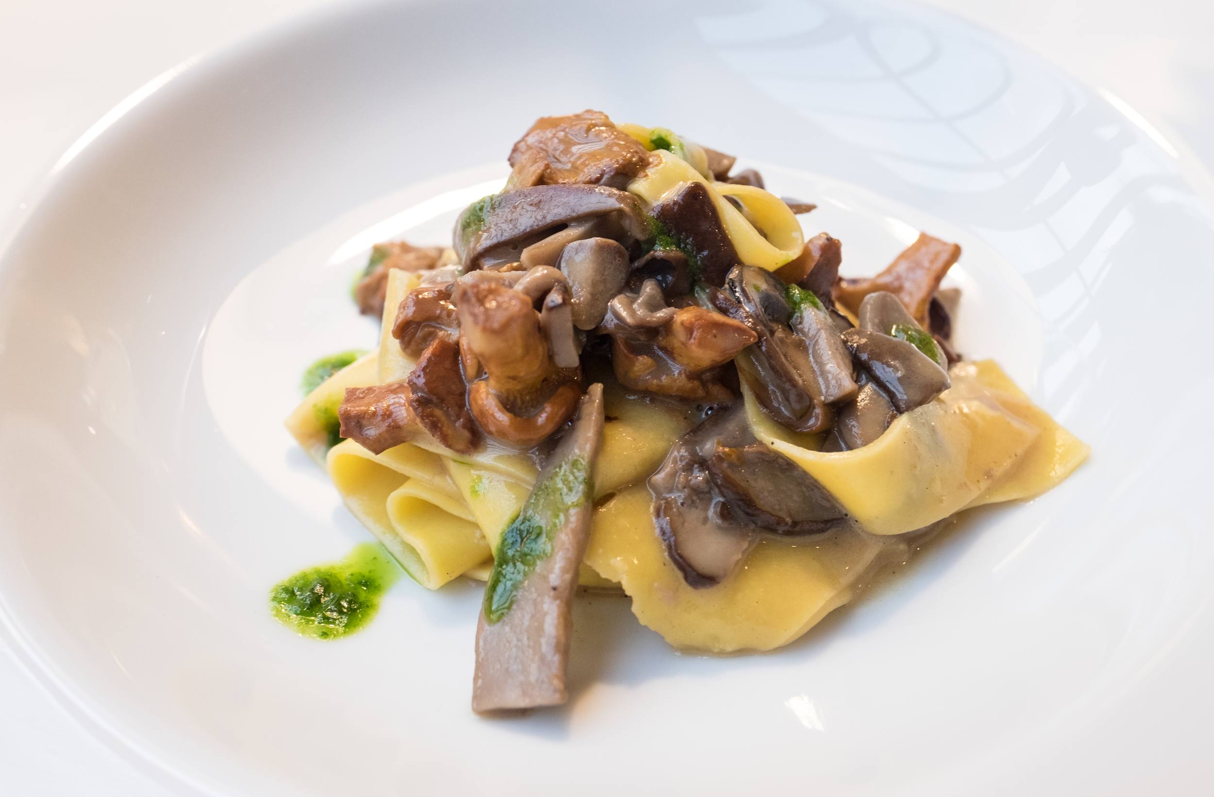 A plate of pappardelle (thick pasta noodles) topped with chanterelle mushrooms.