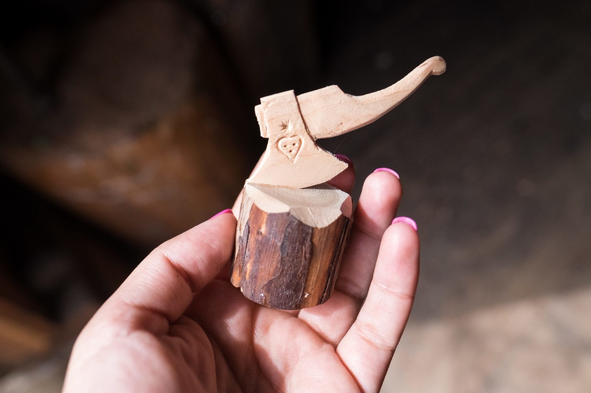 A small wooden carving of an axe in a stump, held in a hand.