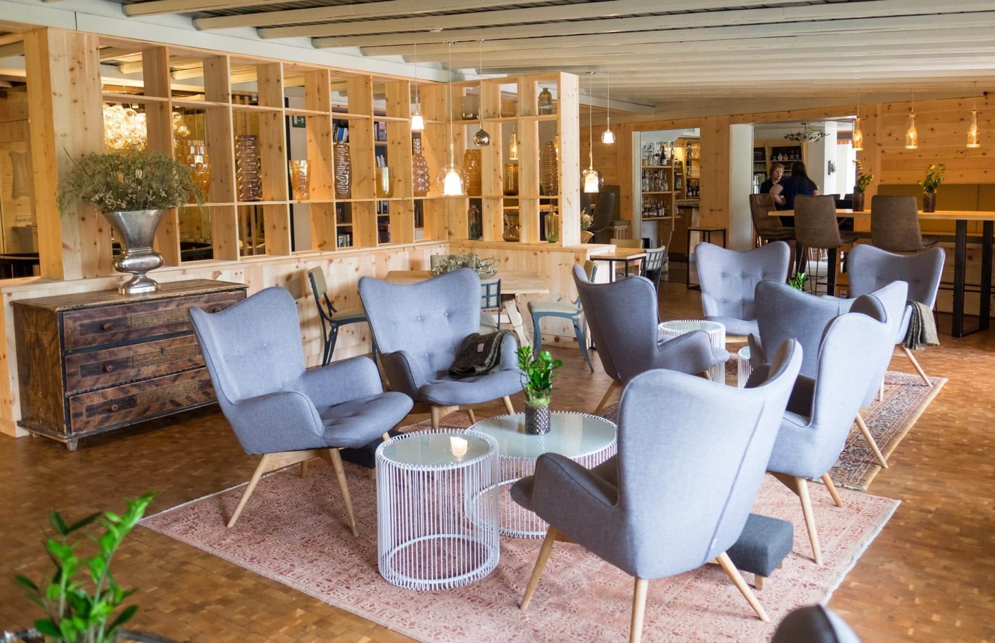 A hotel lobby mixing traditional wooden walls with gray mid-century modern chairs and cage-like metal coffee tables.