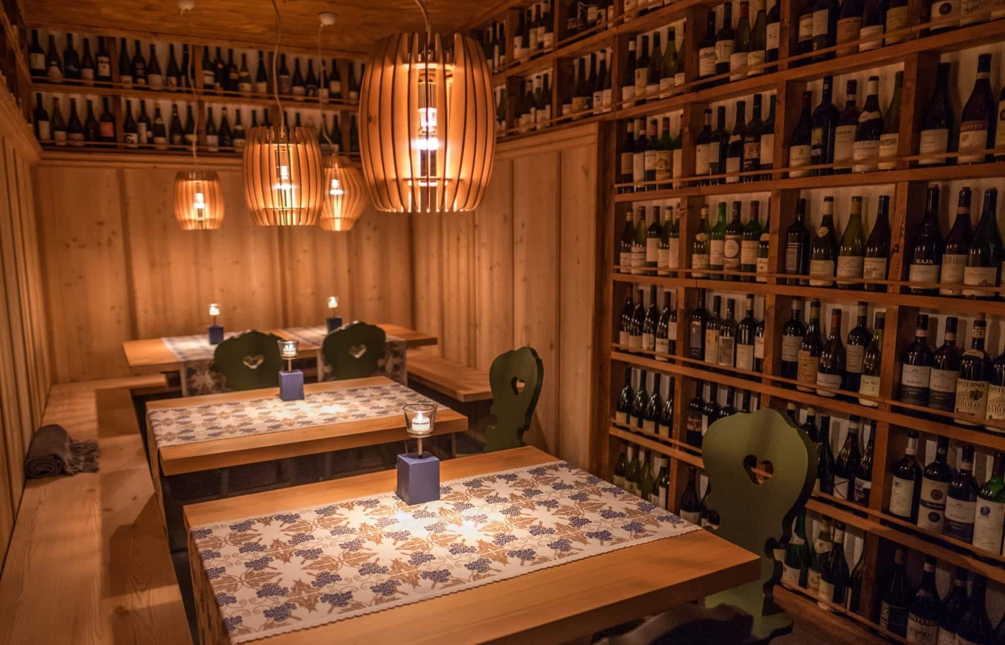 A wine cellar with bottles lining the wood-paneled walls and wooden seats covered with patterned tablecloths.