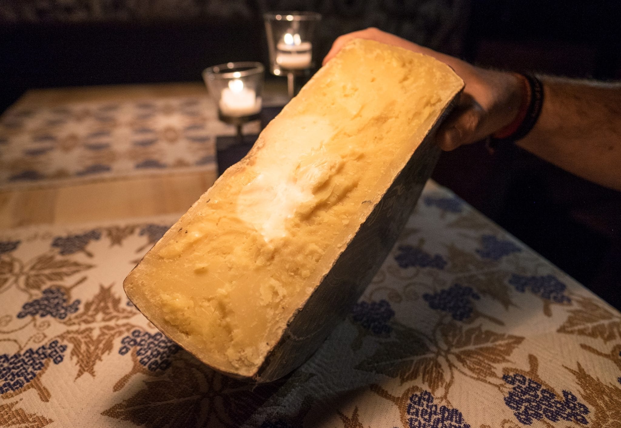 A giant chunk of cheese being held up in the dim light of the wine cellar.