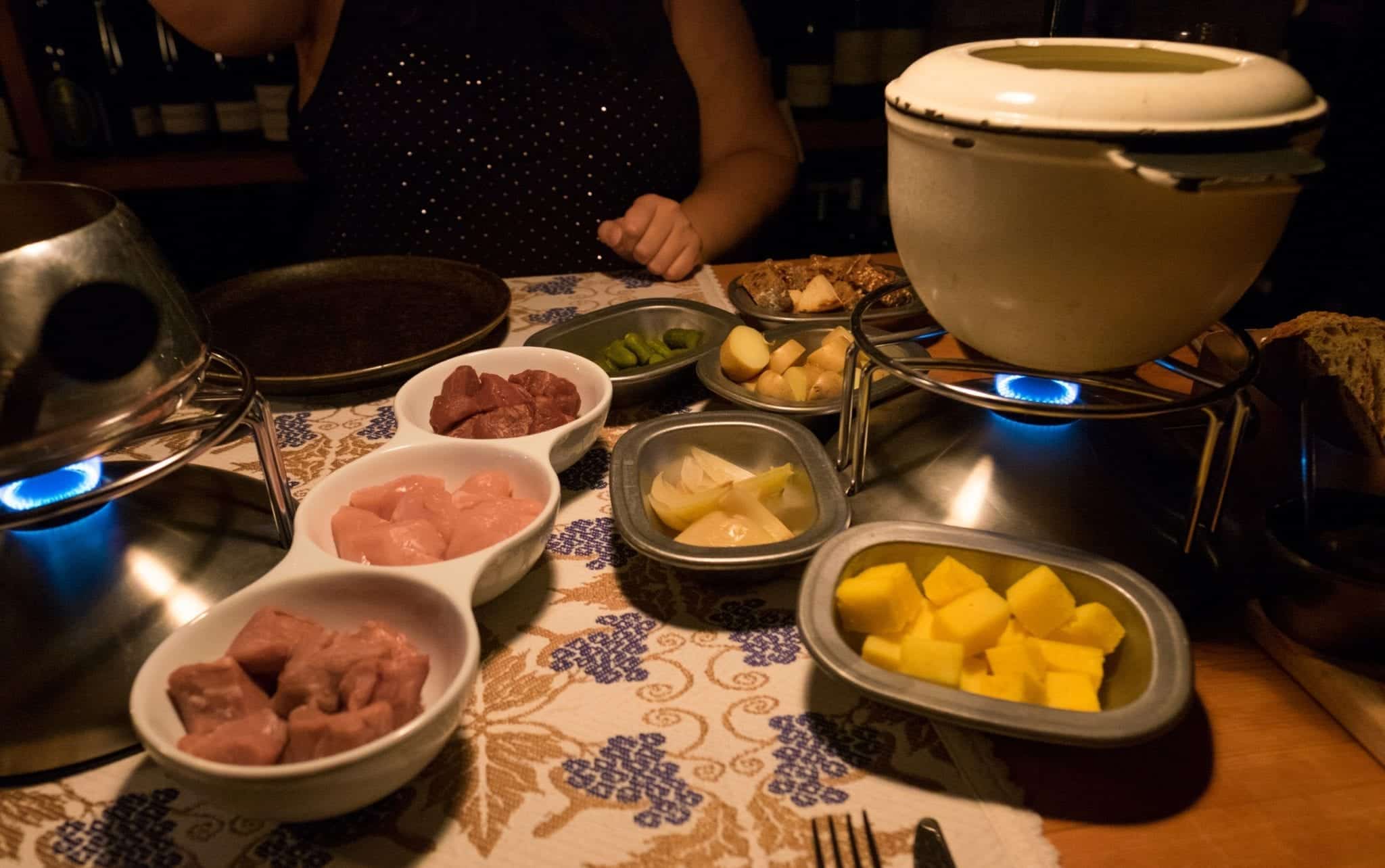 Fondue pots with accoutrements in the front: chicken, veal, and beef, plus polenta, onions, and other small items for dipping.